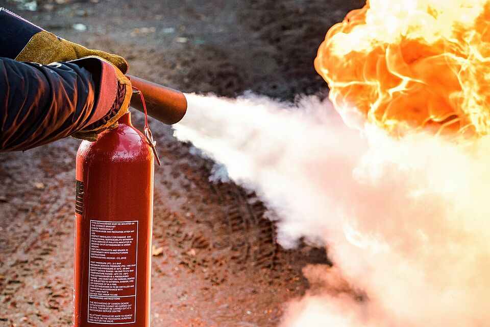 Feuer in der rechten Bildhälfte und ein Feuerlöscher links im Einsatz