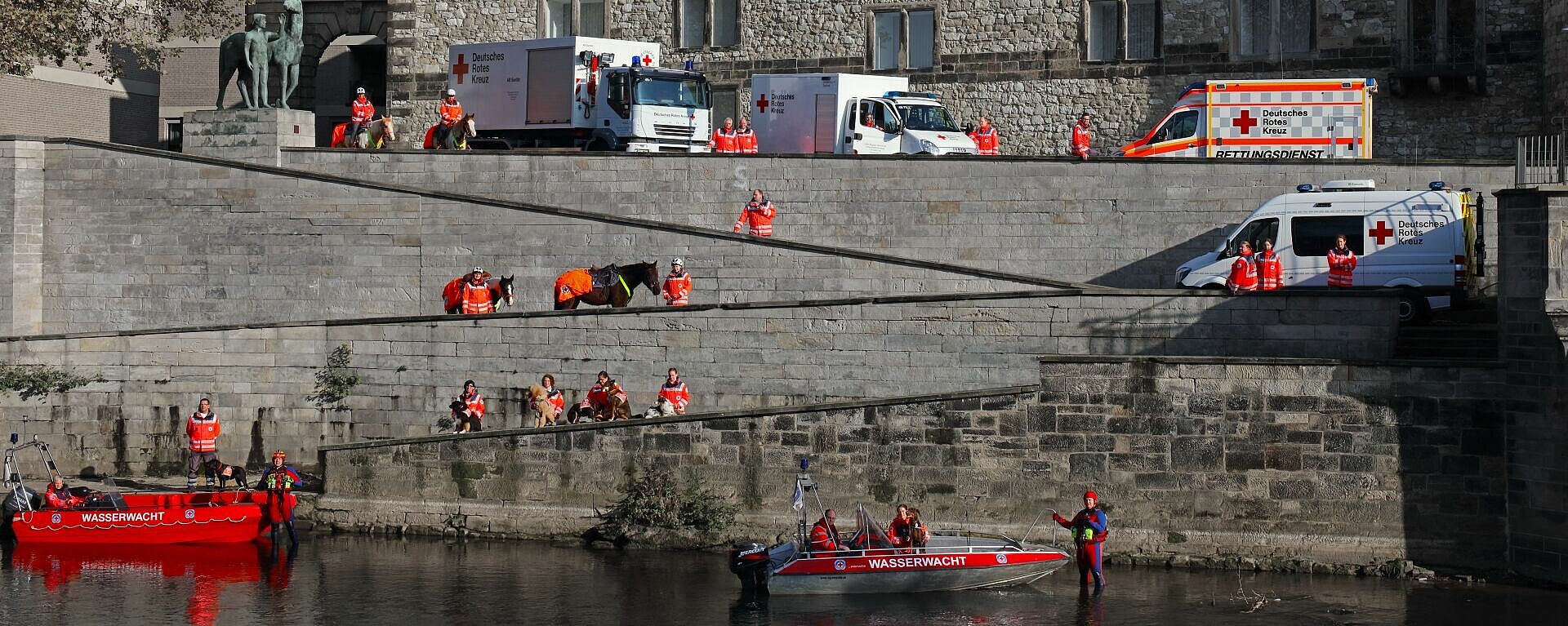 Einsatzkräfte des Deutschen Roten Kreuzes und der Wasserwacht stehen mit Einsatzfahrzeigen, Booten und Pferden am Leineufer Hannover.